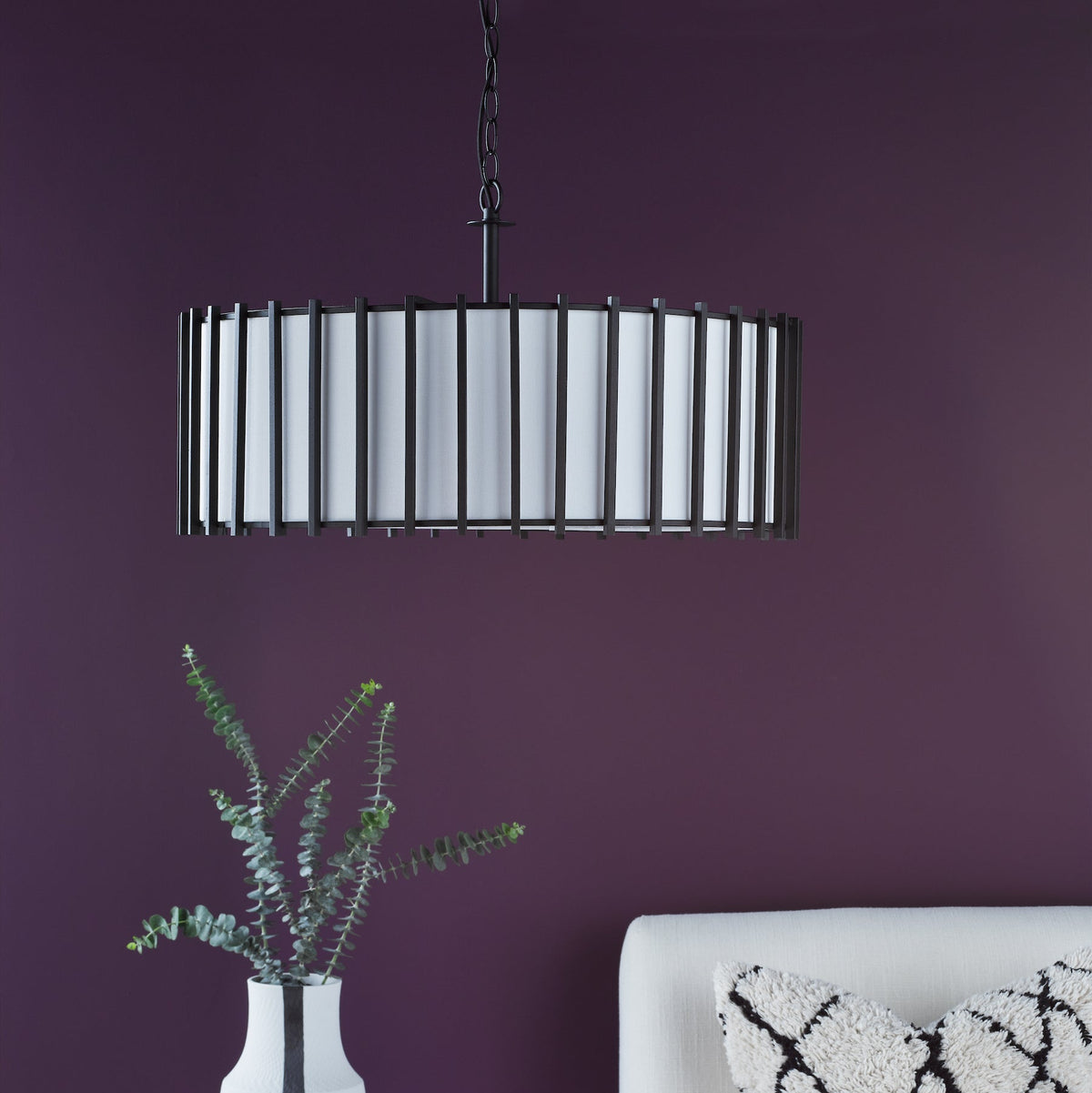 Black metal chandelier with white fabric shade over a white vase with eucalyptus branches
