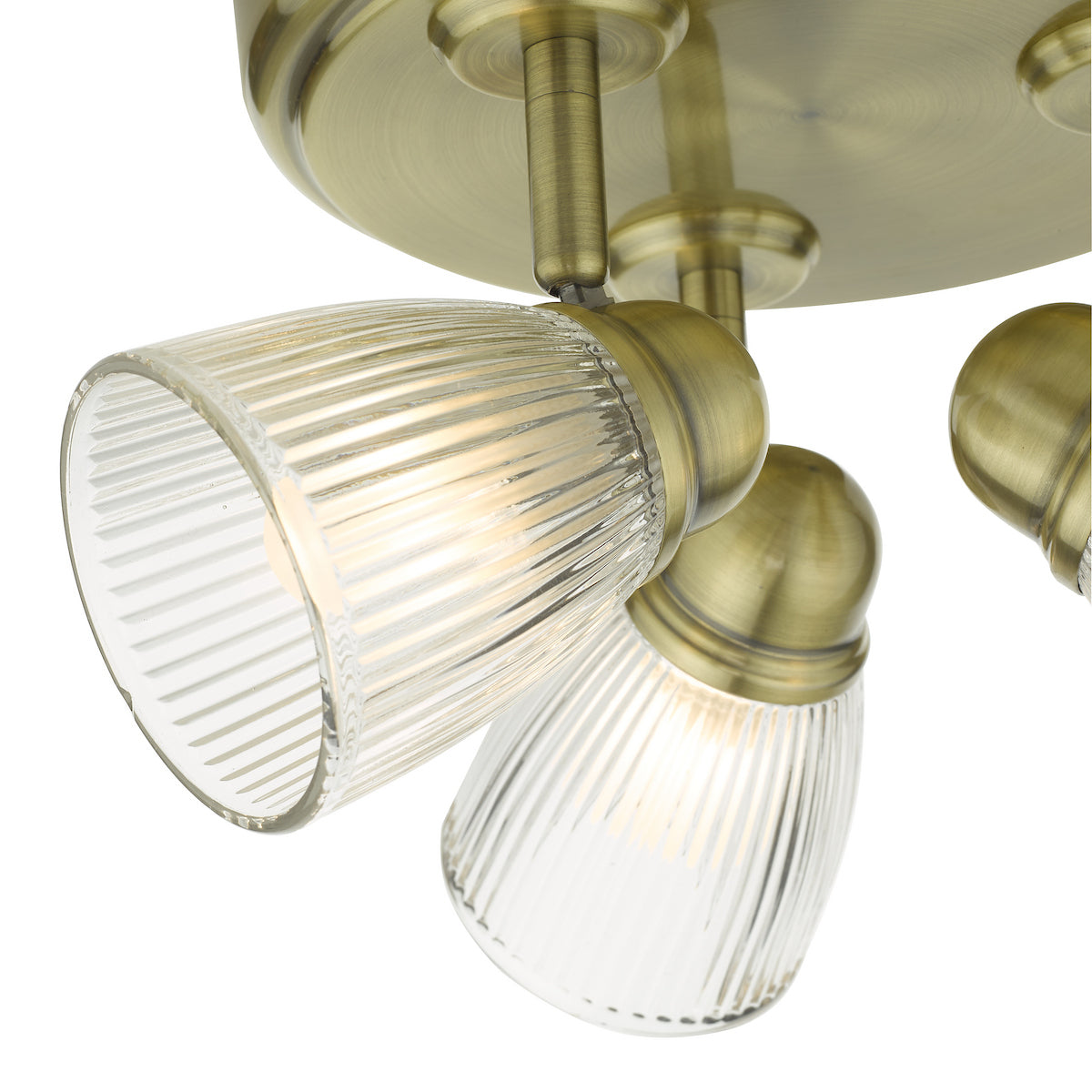 Close-up of a brass ceiling light with three ribbed glass shades, illuminated and angled downwards.