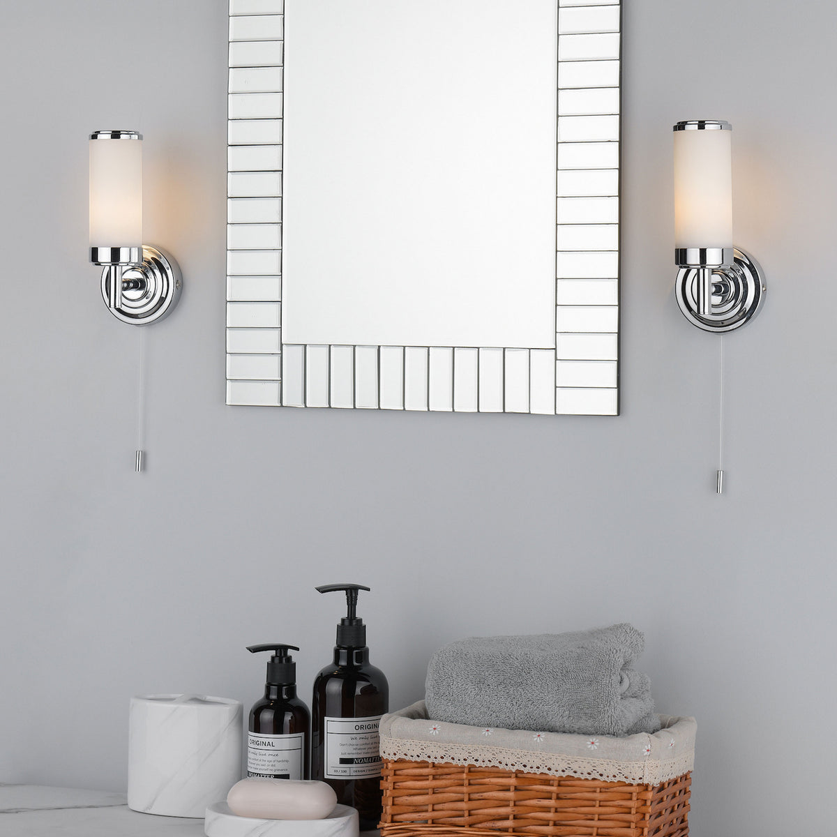 Two chrome wall sconces with frosted glass shades flank a rectangular mirror above a bathroom counter.