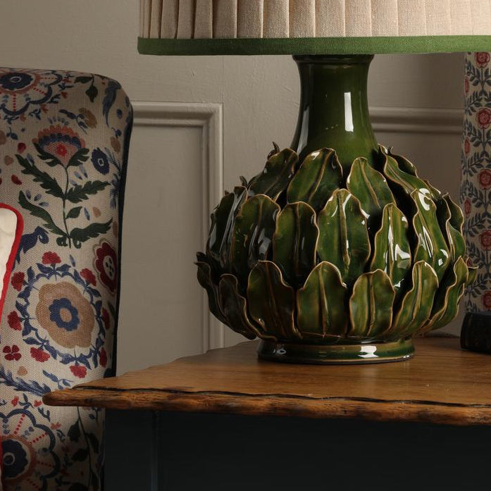 Green ceramic artichoke table lamp with a pleated beige lampshade on a wooden table