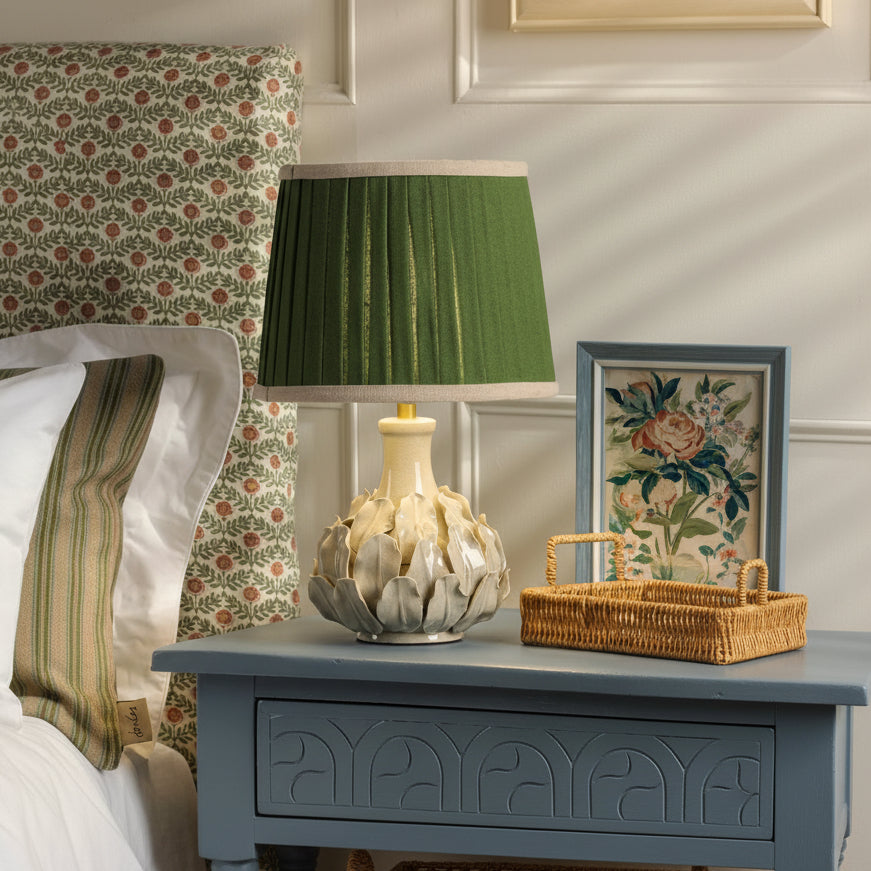 Joules Chatsworth ceramic table lamp in cream with a pleated green linen shade on a blue bedside table