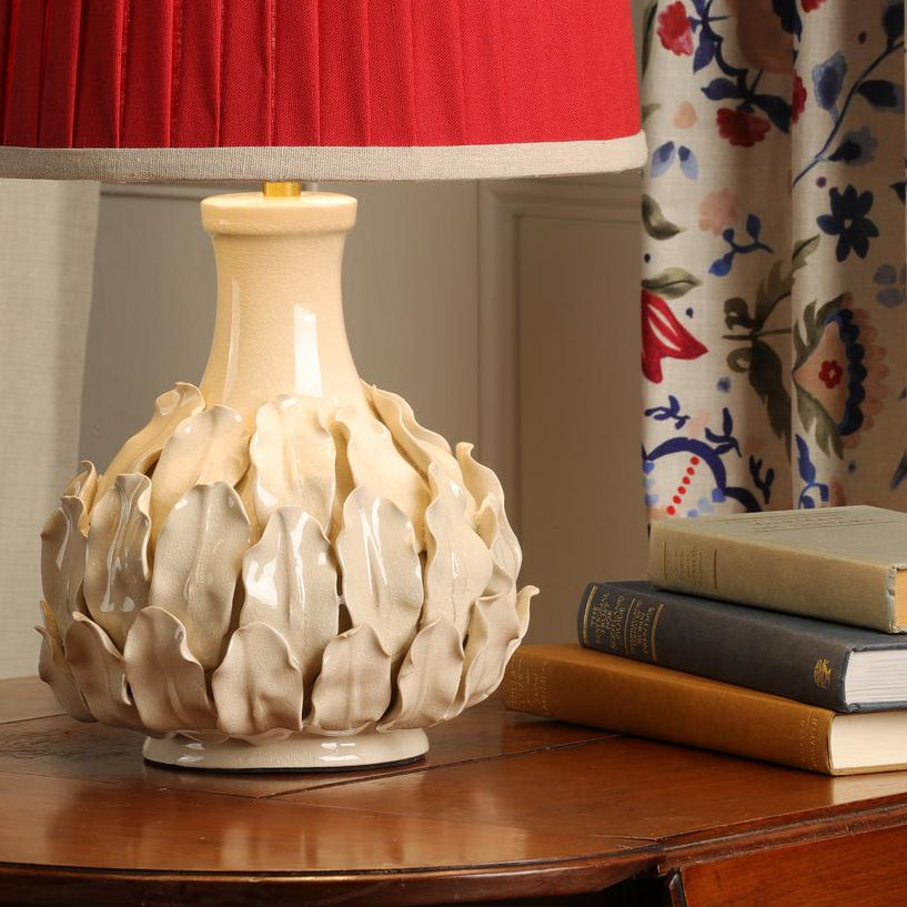 Cream ceramic table lamp with leaf texture base and red pleated shade on wooden table