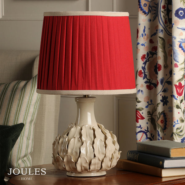 Joules Home table lamp with a red pleated shade and a cream ceramic base featuring a leaf design