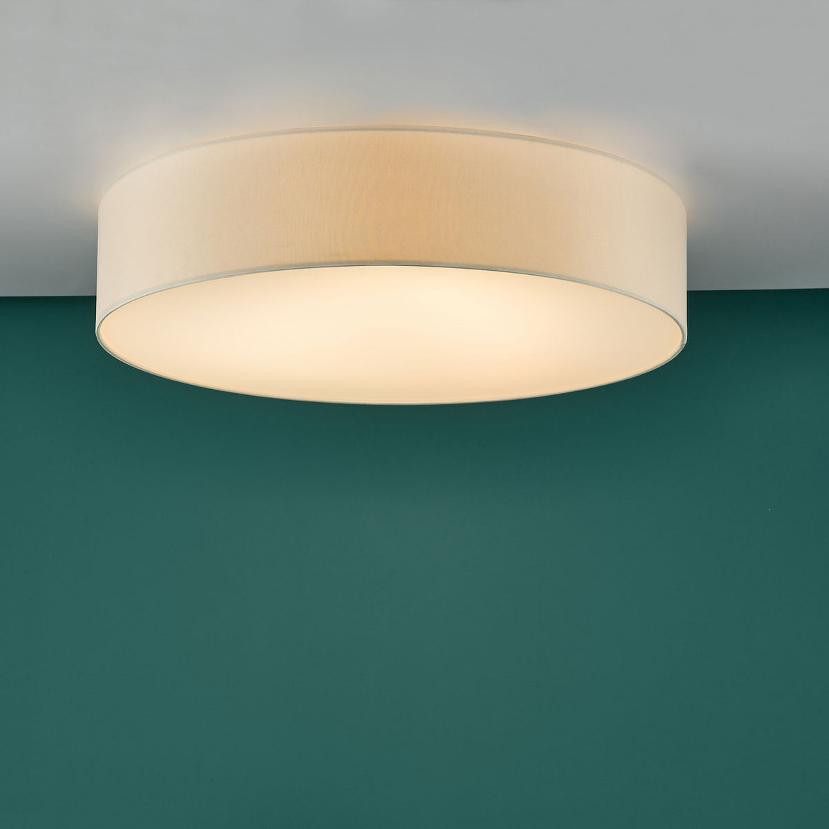A round, cream-colored fabric ceiling light illuminates a teal wall.
