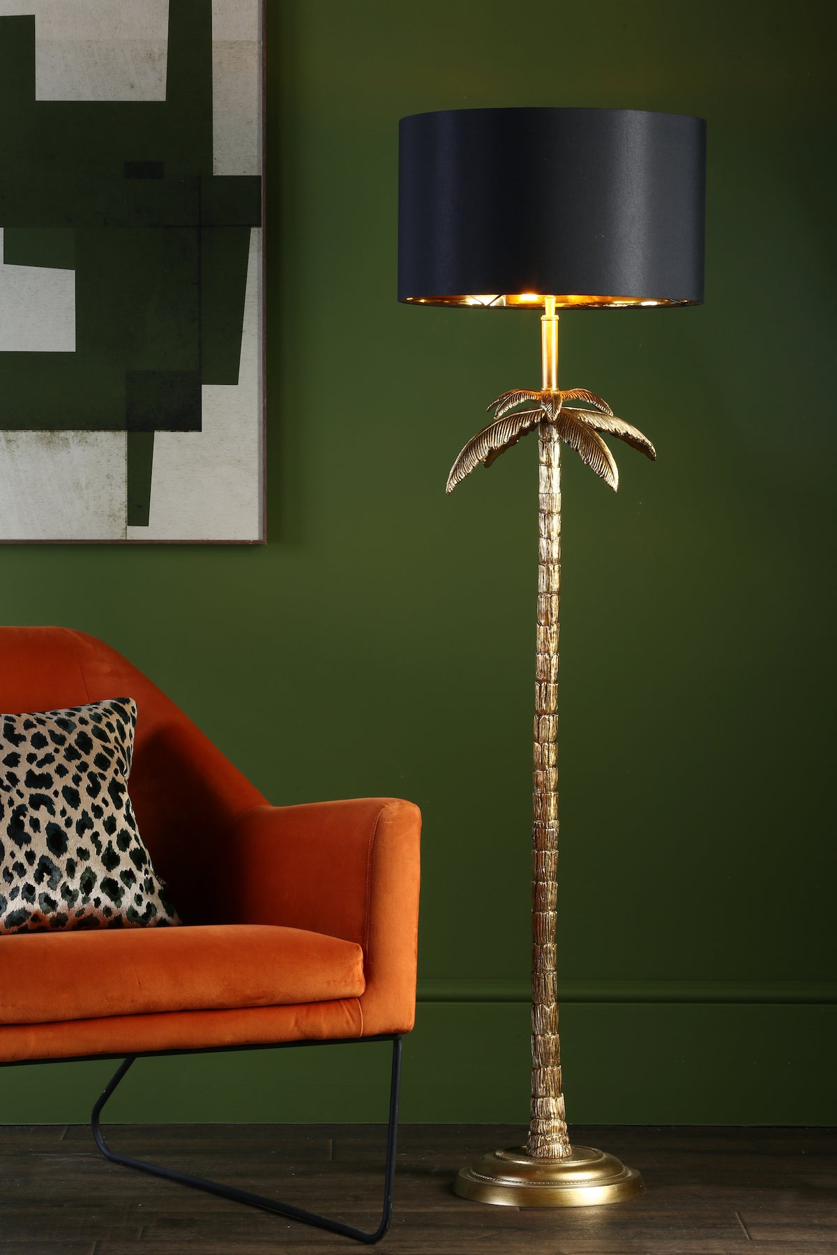 Golden palm tree floor lamp with black shade next to an orange armchair with a leopard print cushion.