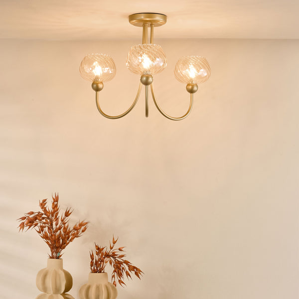 Three-light gold ceiling fixture with textured glass shades illuminating a light-colored wall