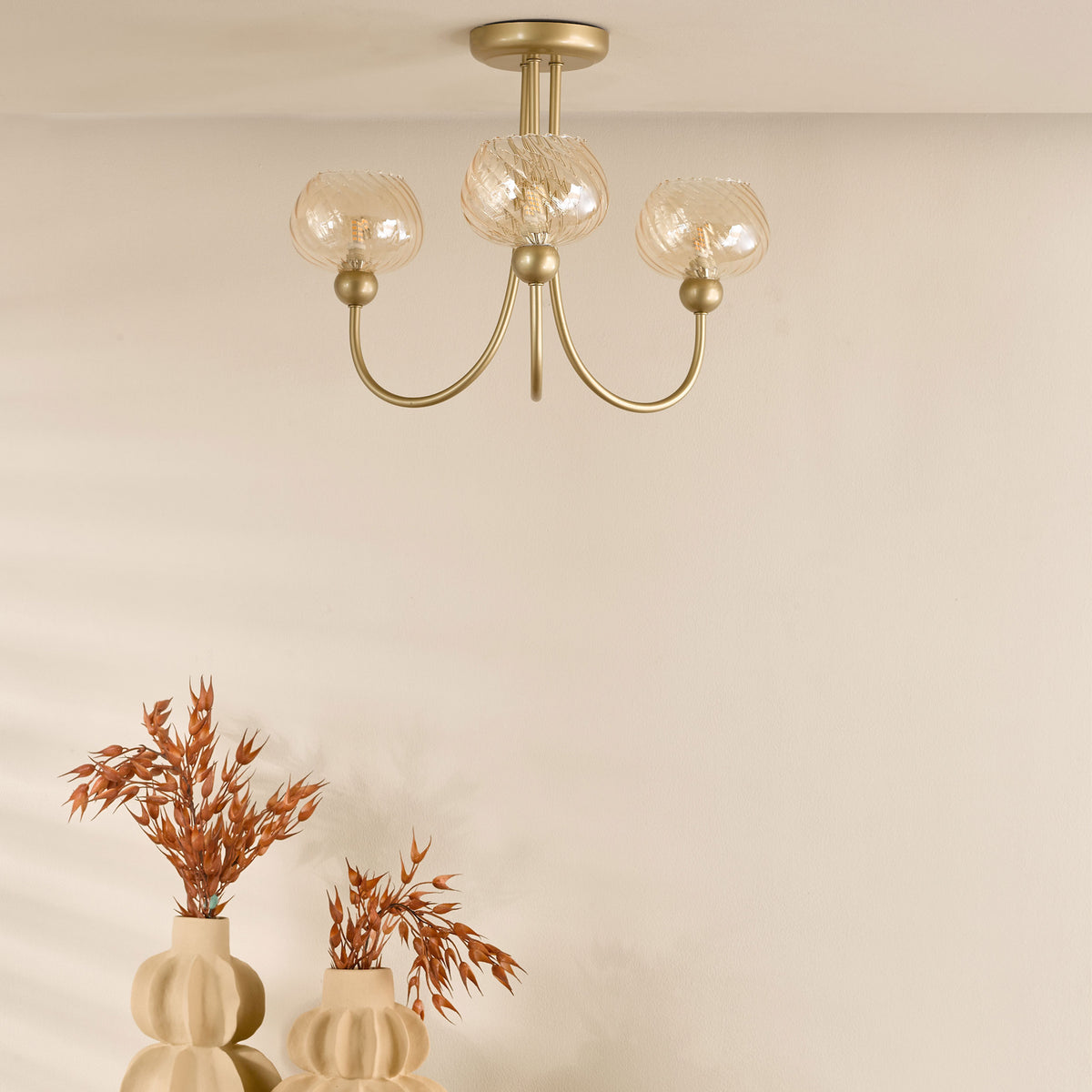 Gold chandelier with three textured glass shades, above two beige vases with dried orange foliage