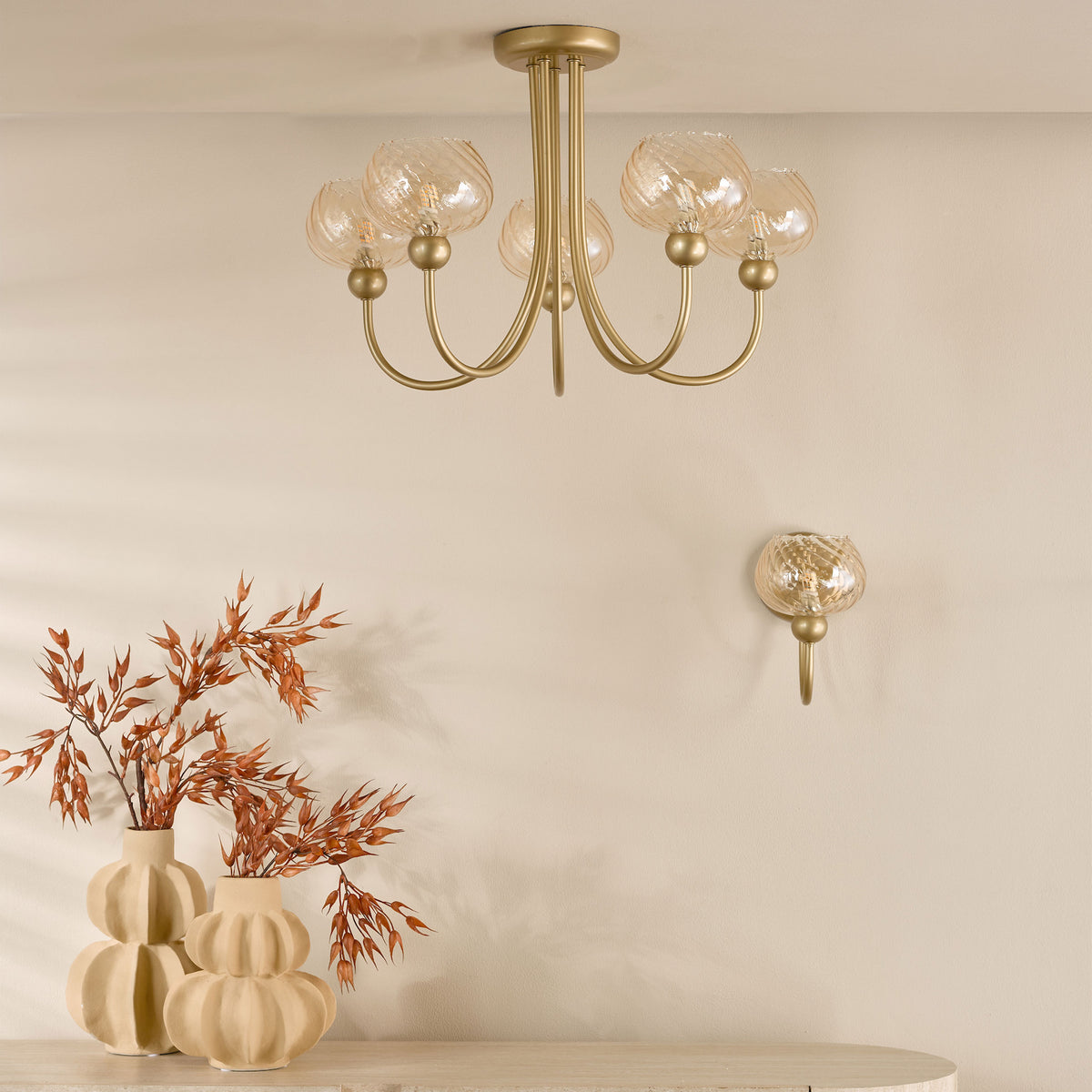Gold chandelier with five glass globes, a matching wall sconce, and two beige vases with dried plants