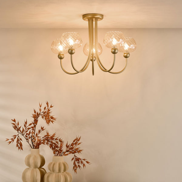 Gold chandelier with five clear glass shades and two cream vases with dried branches