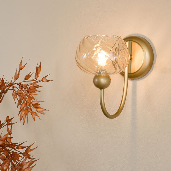 Gold wall sconce with a clear, textured glass shade and a visible light bulb