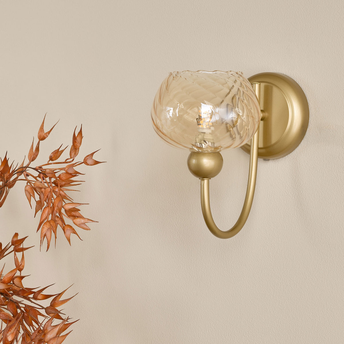 Gold wall sconce with a textured amber glass shade and a decorative branch with dried seed pods