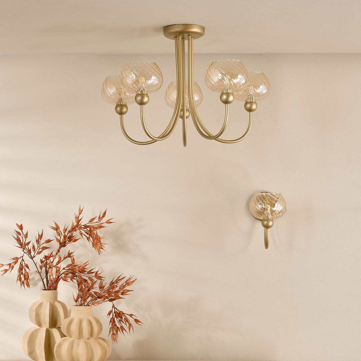Gold chandelier with five amber glass shades and a matching wall sconce above two beige vases with dried plants