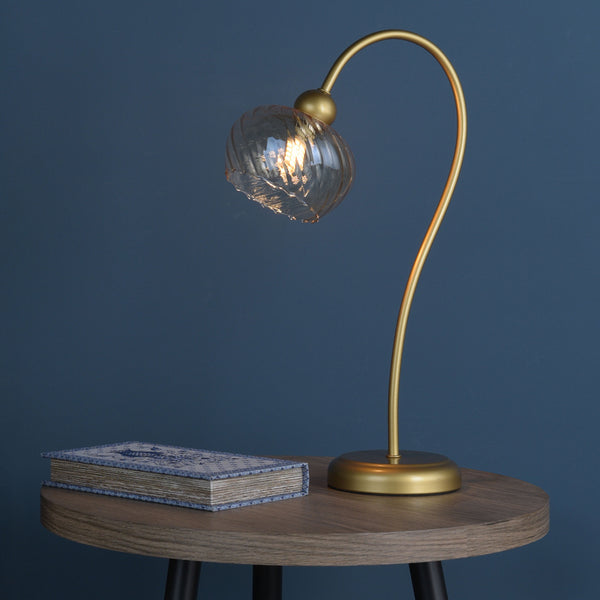 Gold table lamp with a clear glass shade and a book with a blue and white cover on a wooden table