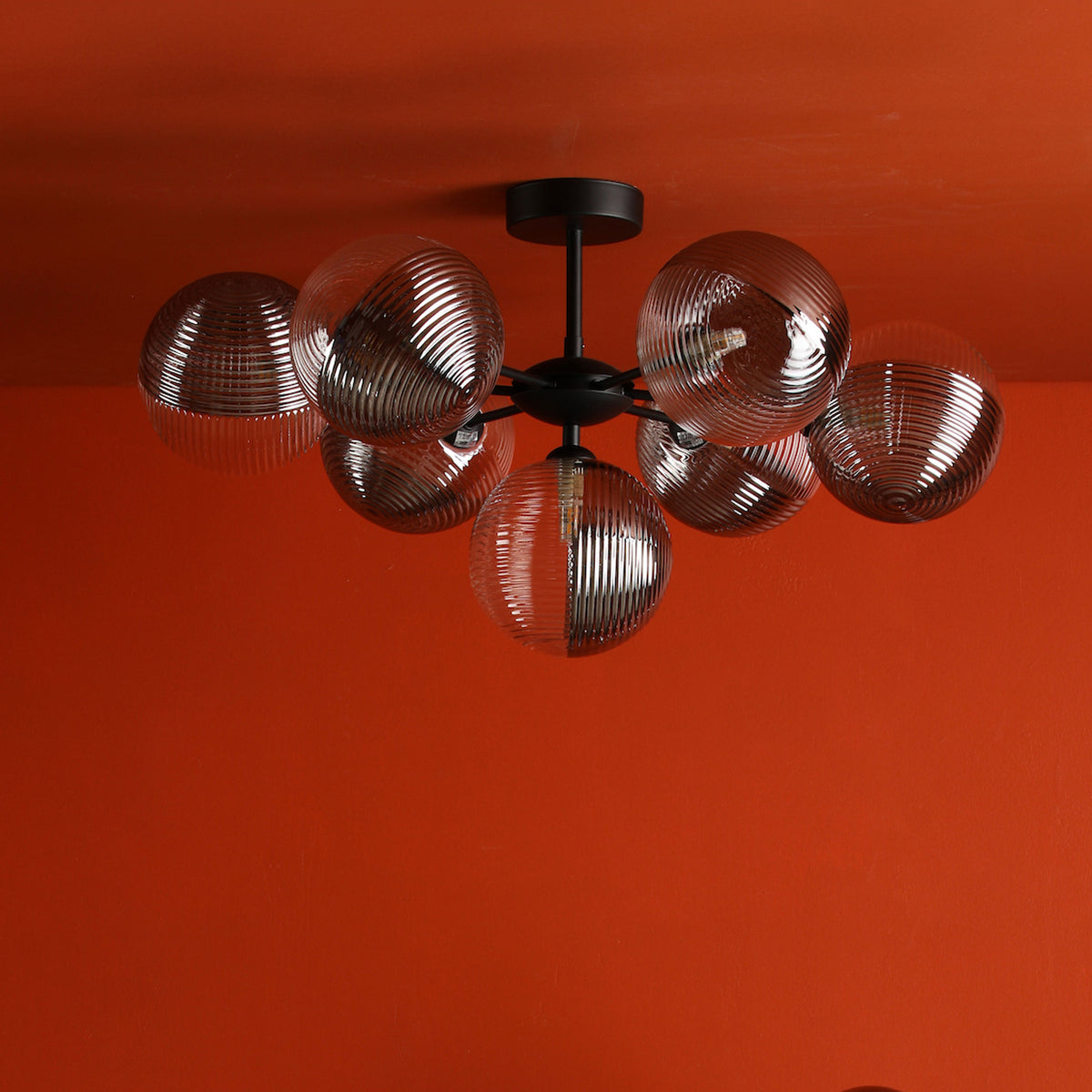 Modern black chandelier with six clear, ribbed glass globe shades against a vibrant orange wall.