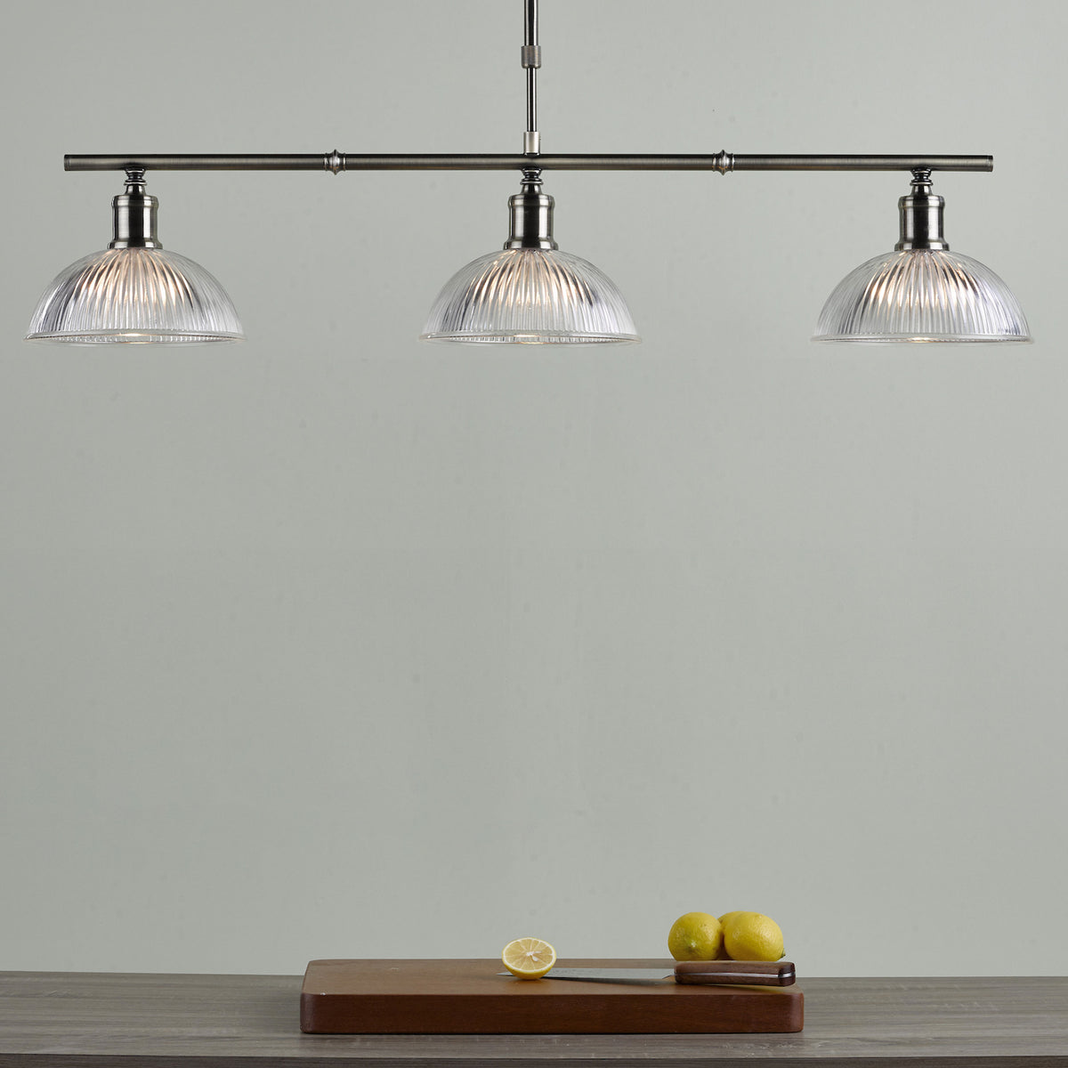 Three clear glass dome pendant lights hang above a wooden cutting board with lemons and a knife.