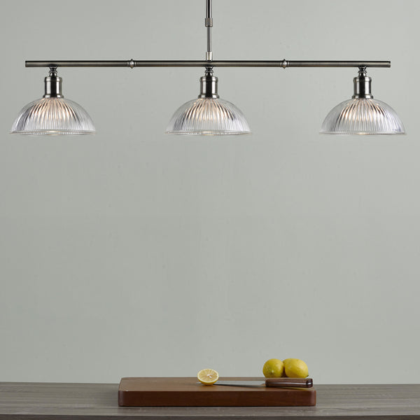 Three clear glass dome pendant lights hang above a wooden cutting board with lemons and a knife.