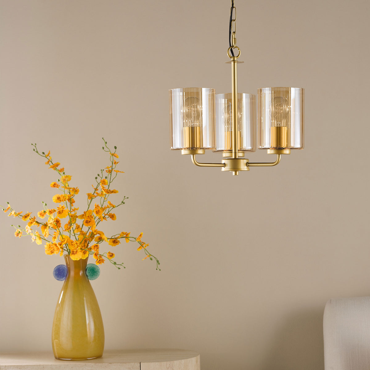 Three-light chandelier with amber glass shades and a vase of yellow flowers on a table