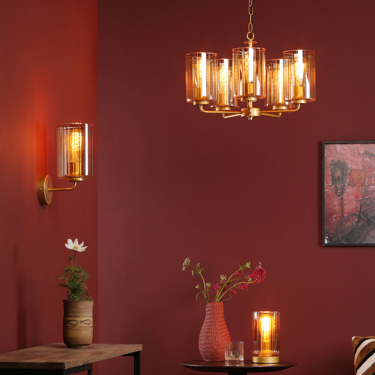 A room with a red wall, a chandelier, a wall lamp, a table lamp, and two vases with flowers