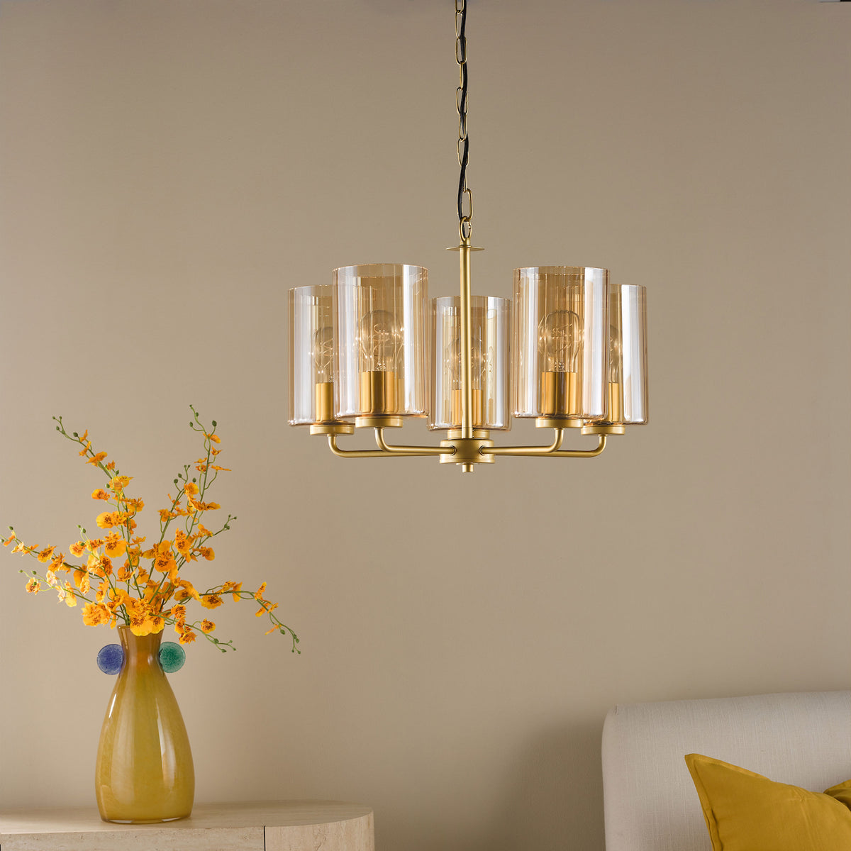 Gold chandelier with amber glass shades hanging above a vase of yellow flowers and a white headboard