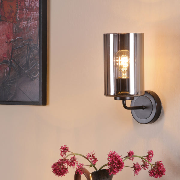 Wall-mounted light fixture with a ribbed glass shade and an exposed bulb