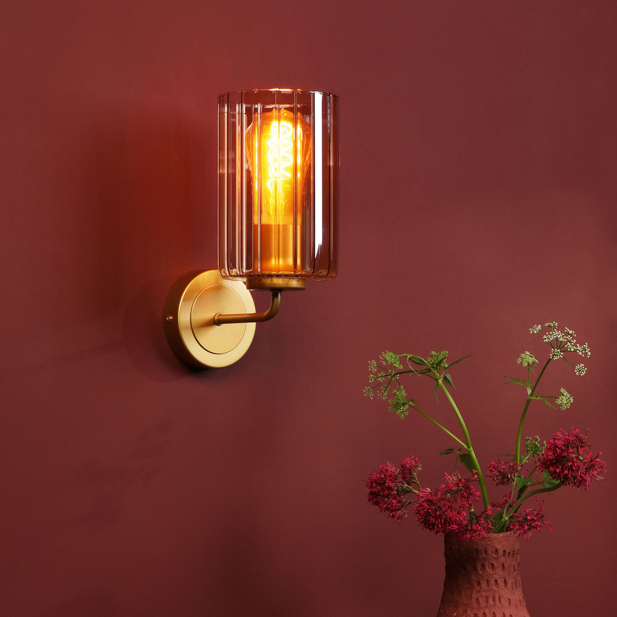 Brass wall light with a fluted glass shade and an exposed filament bulb
