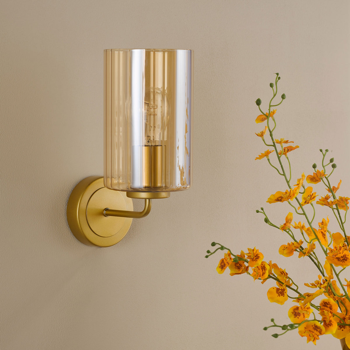 Gold wall sconce with a ribbed amber glass shade and an exposed bulb, next to yellow flowers