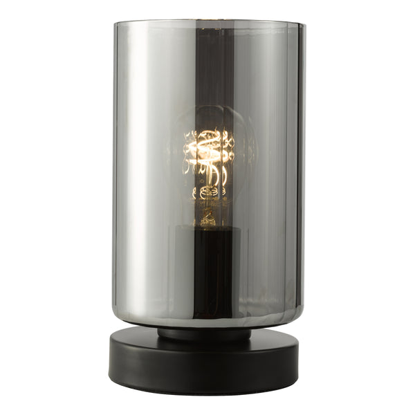 Cylindrical table lamp with a black base and a smoked glass shade, revealing a glowing spiral filament bulb