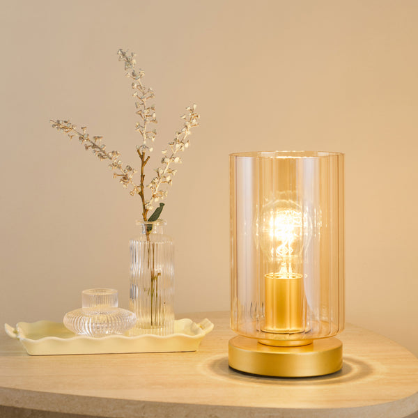 Table lamp with a ribbed amber glass shade and a gold base, next to a clear ribbed vase with dried flowers