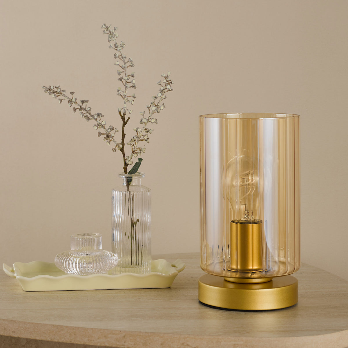 Table lamp with a gold base and ribbed glass shade, next to a vase with white flowers on a light yellow tray