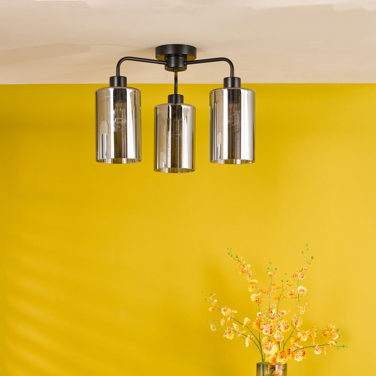 Three-light ceiling fixture with smoked glass shades and a black metal frame, against a yellow wall