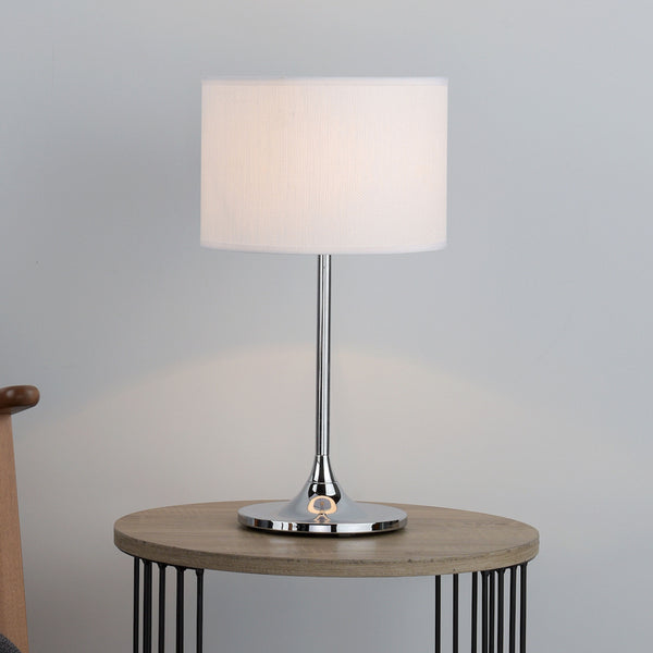 Modern table lamp with a white fabric shade and a polished chrome base on a wooden side table.