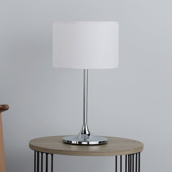 A modern table lamp with a white fabric shade and a polished chrome base on a light wooden side table.