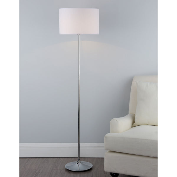 A chrome floor lamp with a white drum shade next to a cream armchair on a wooden floor.