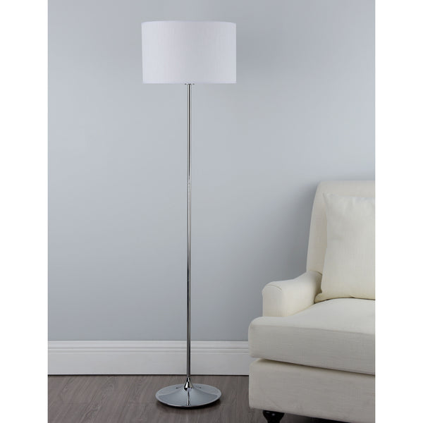 A chrome floor lamp with a white drum shade next to a cream armchair on a wooden floor.