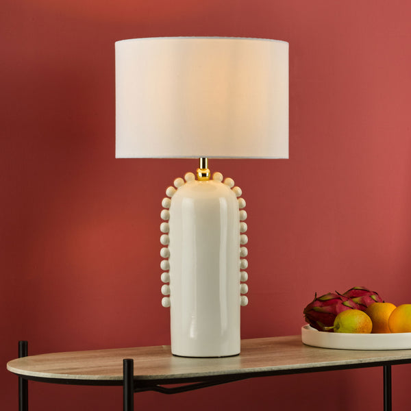 White table lamp with a textured base and a white shade, next to a bowl of fruit.