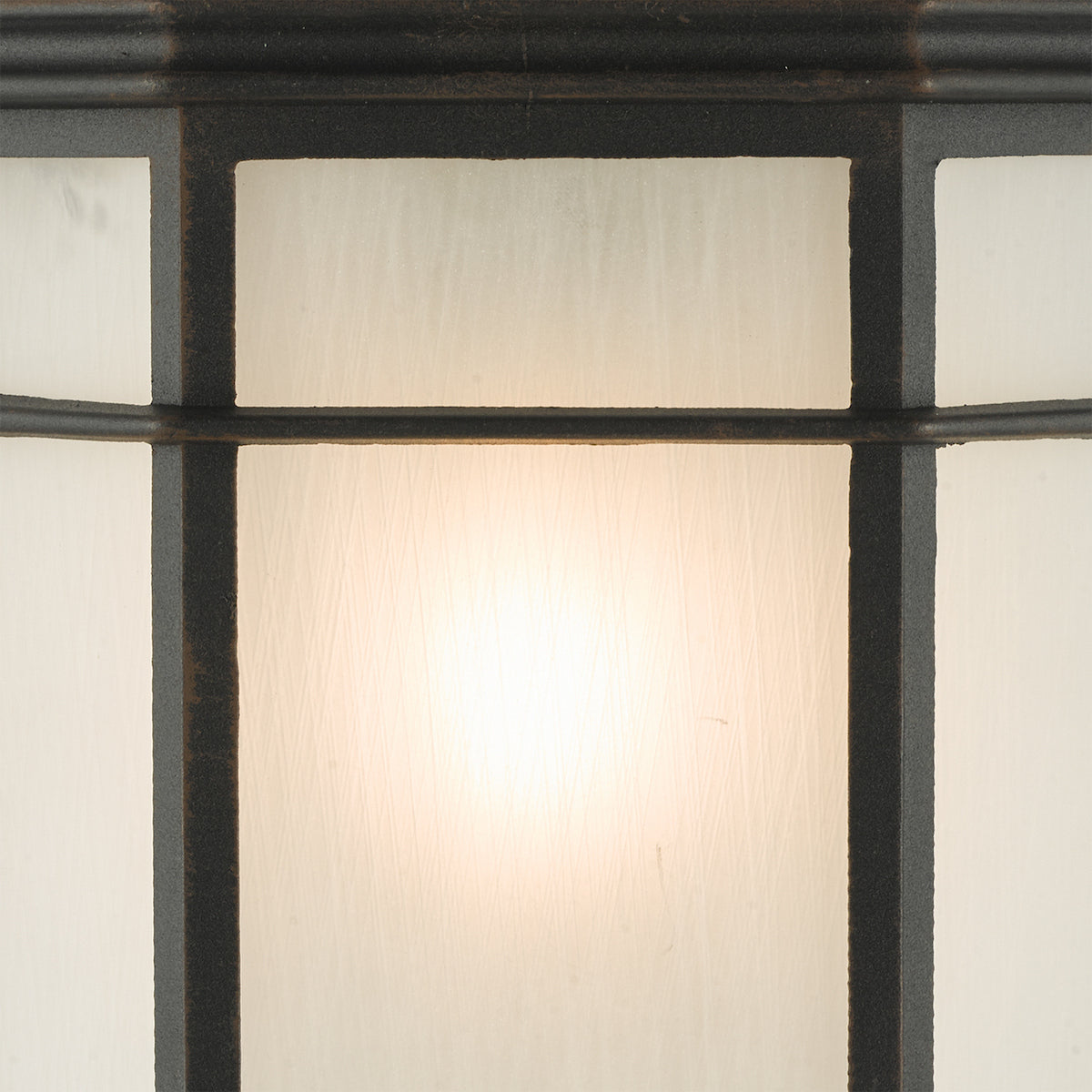 Close-up of a frosted glass light fixture with a dark metal frame, glowing softly.