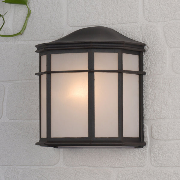 Dark bronze outdoor wall light with frosted glass panels, mounted on a white brick wall.