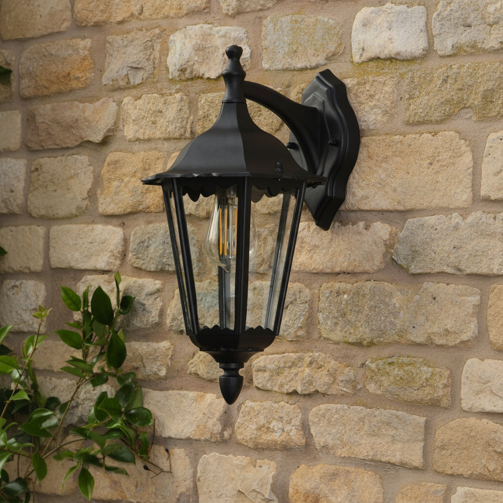 Black outdoor lantern with clear glass panels and an exposed filament bulb, mounted on a stone wall