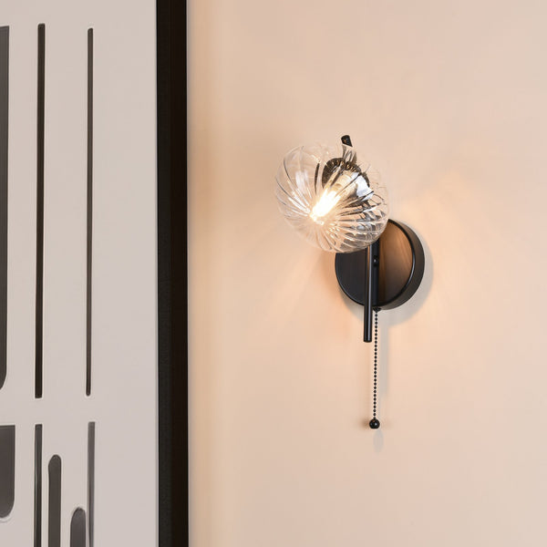 Black wall sconce with a clear, ribbed glass shade and a pull chain switch