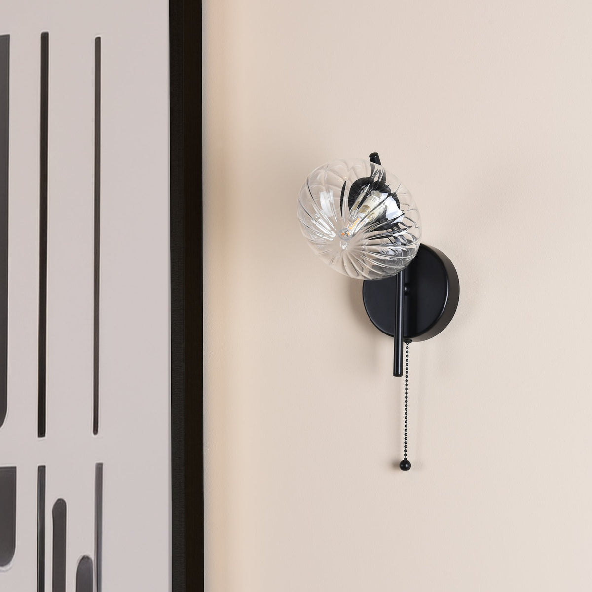 Black wall sconce with a clear, ribbed glass shade and a pull chain switch