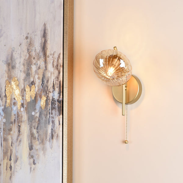 Gold wall sconce with a fluted glass shade and pull chain next to an abstract painting