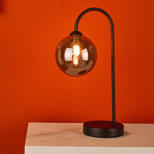 Black metal table lamp with a round smoked glass shade and exposed bulb on a white marble surface