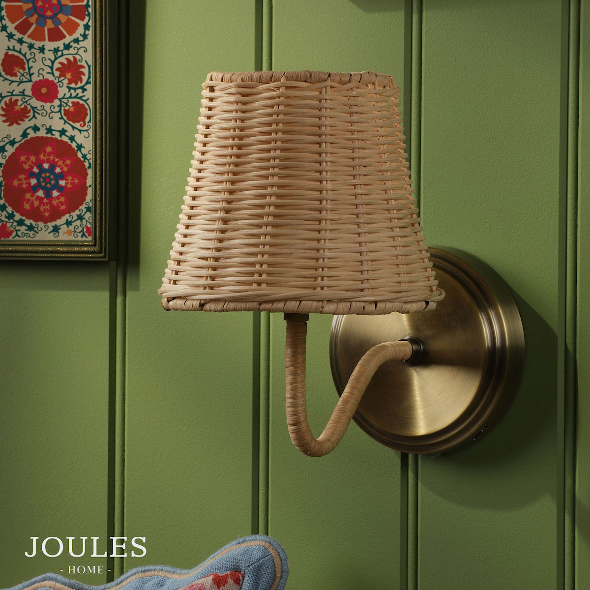 Joules Home wall light with a woven rattan shade and antique brass fixture on a green paneled wall