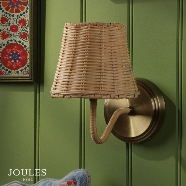 Joules Home wall light with a woven rattan shade and antique brass fixture on a green paneled wall