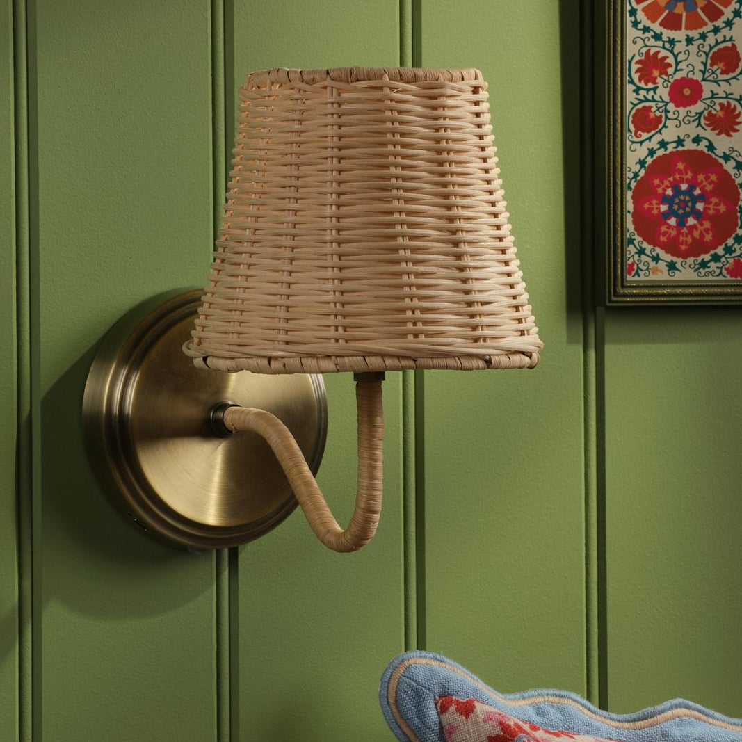 Joules Elcot rechargeable wall light with antique brass base and natural rattan shade mounted on a green wall