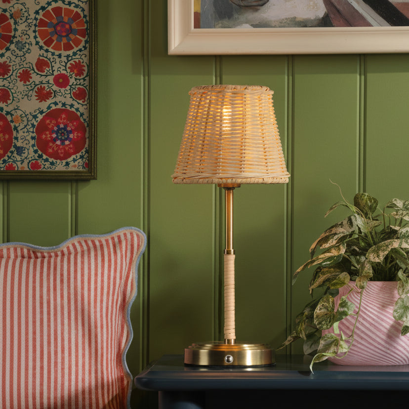 Table lamp with a woven rattan shade and brass base on a dark blue surface