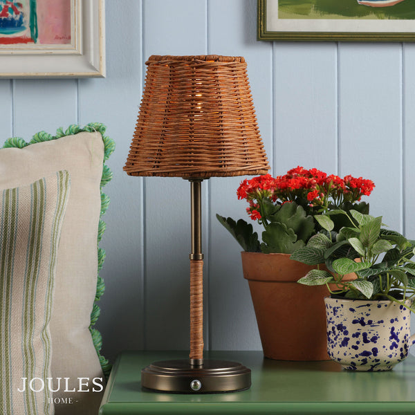 Joules Home table lamp with a woven rattan shade and metal base on a green surface
