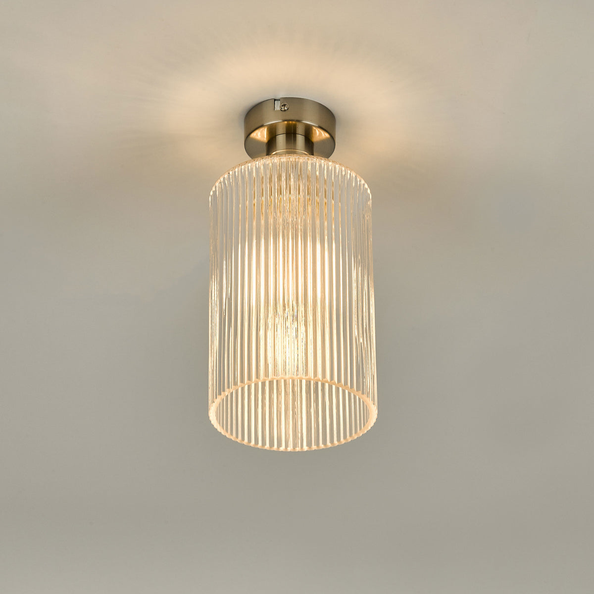 A modern ceiling light with a brushed nickel base and a ribbed glass cylindrical shade, emitting a warm glow.