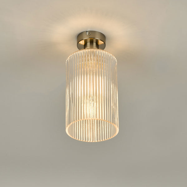 A modern ceiling light with a brushed nickel base and a ribbed glass cylindrical shade, emitting a warm glow.