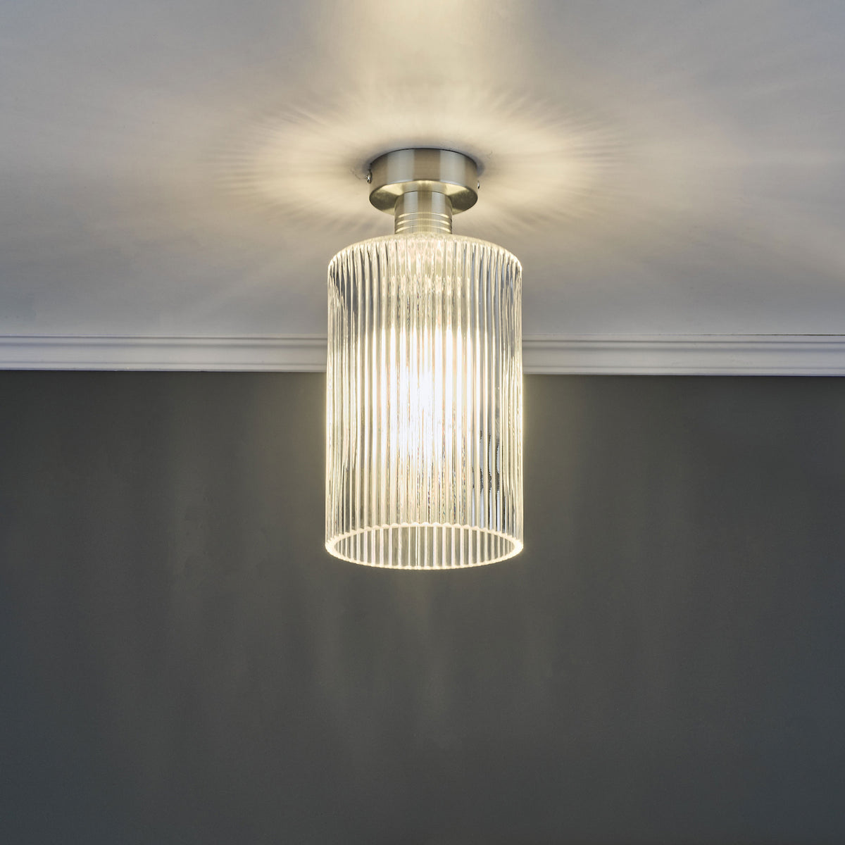 A modern ceiling light with a brushed nickel base and a fluted glass shade, casting light upwards.
